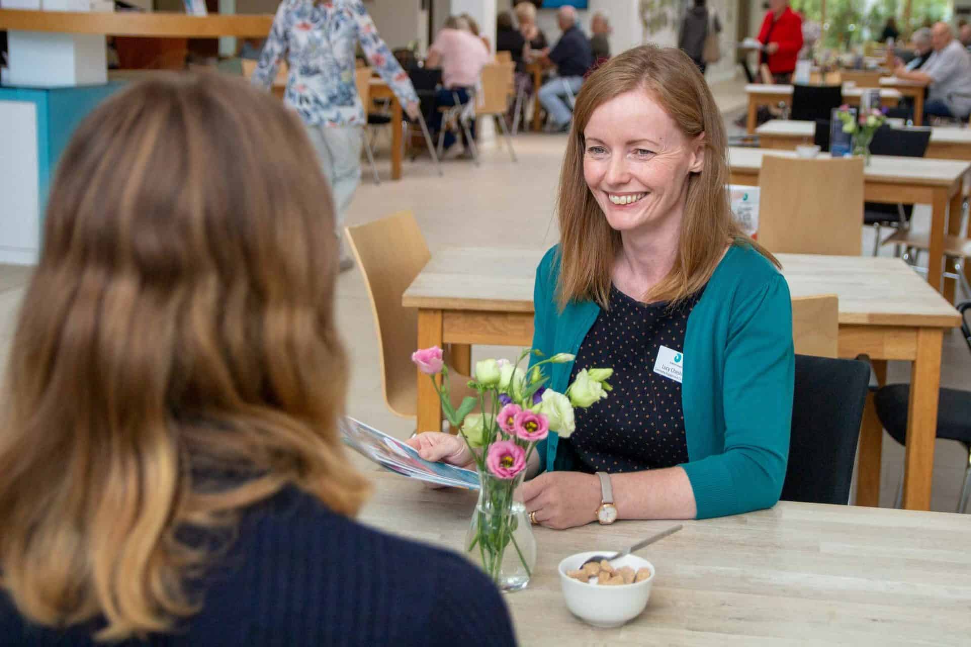 Contact Us Smiling woman talking and sharing leaflets with friend at hospice