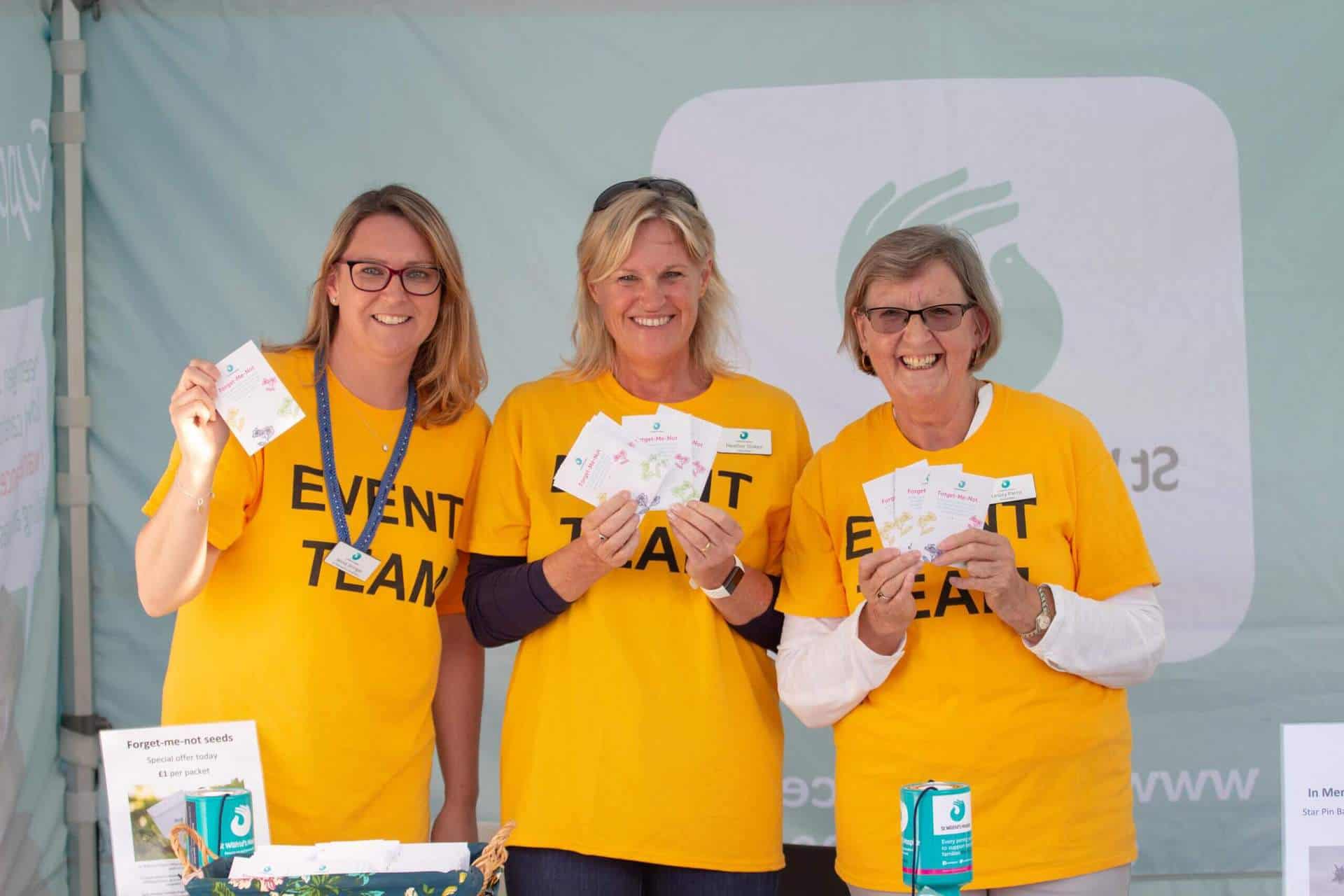 Three volunteers holding packets of seeds smiling at camera