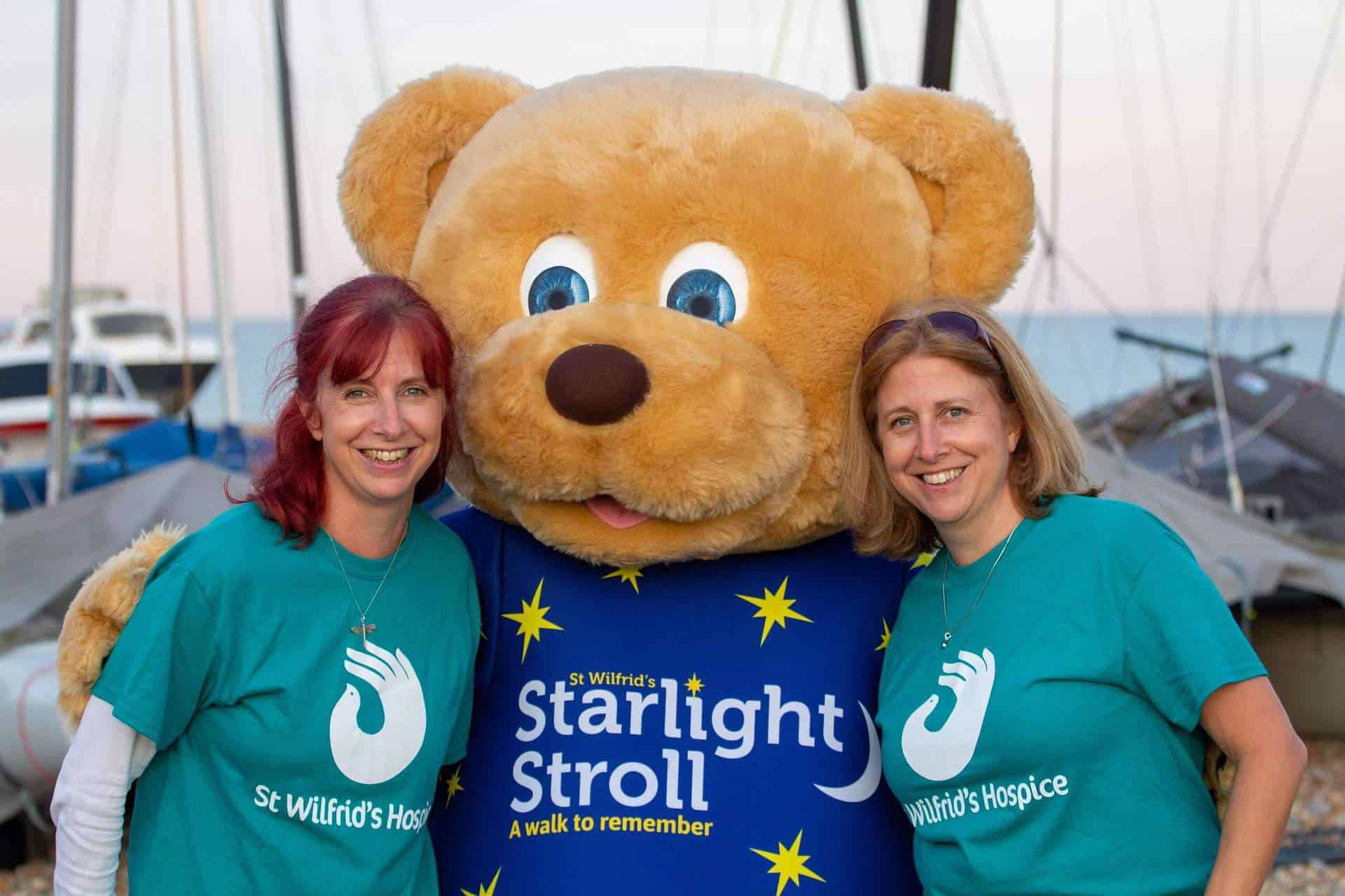 Wilfie Bear in Starlight Costume with two volunteers smiling at camera