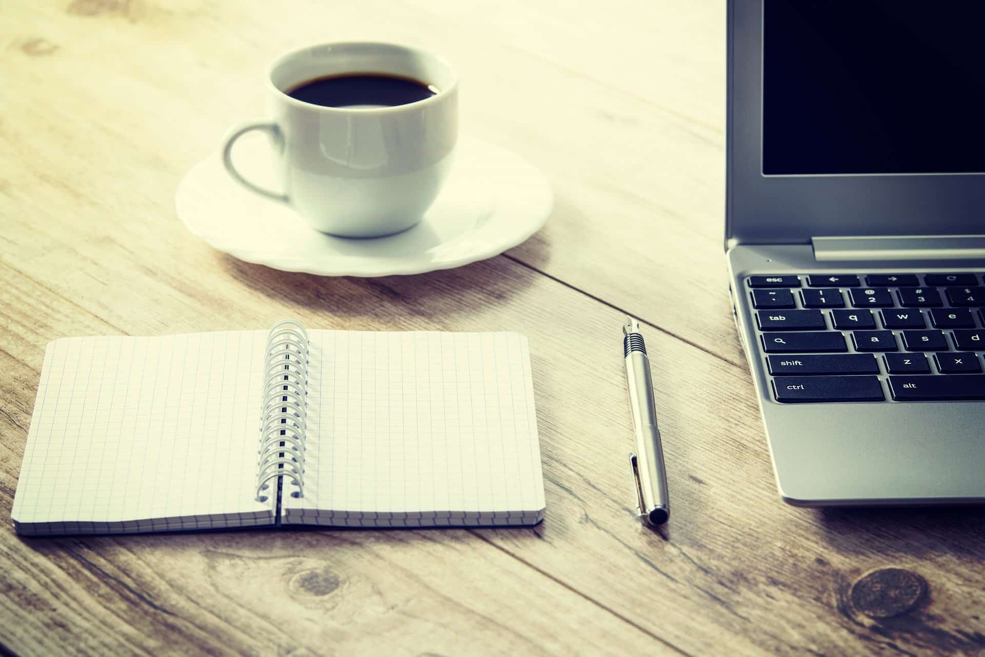 Working scene - laptop, open notebook, pen and coffee on wooden table