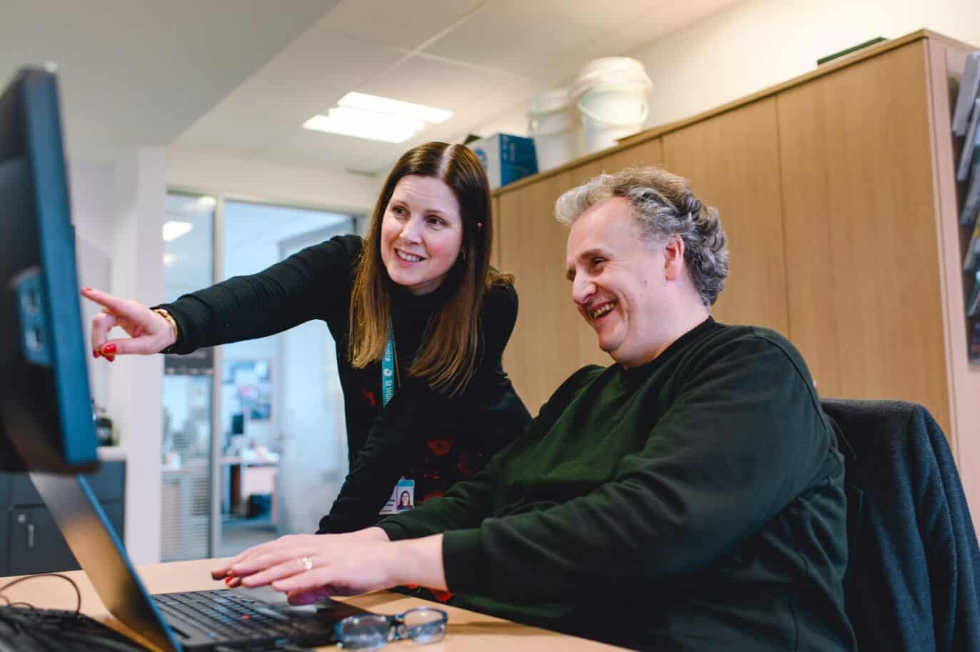 two people smiling and pointing at a computer