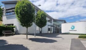 A view of the front of the hospice building, with trees lining the path, and the white building in the background.