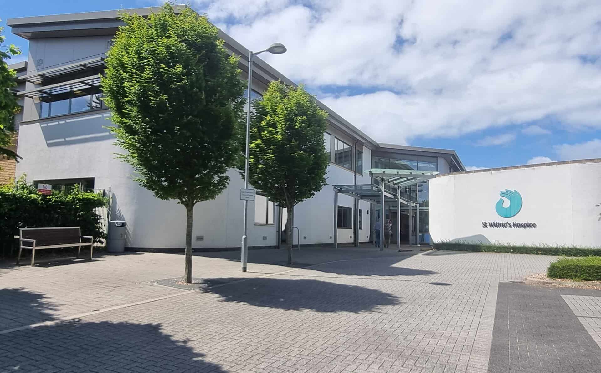 A view of the front of the hospice building, with trees lining the path, and the white building in the background.